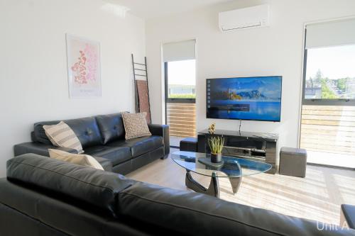 a living room with a black leather couch and a tv at Modern Howick Town House Fibre WiFi Netflix in Auckland