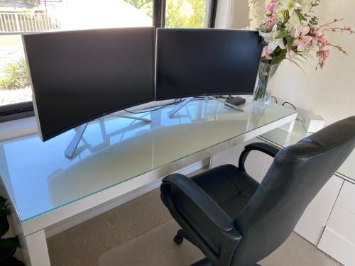 a glass desk with a computer monitor and a chair at HEATed Pool, Lake & Beach, Luxury 5 B/R House in Lake Illawarra