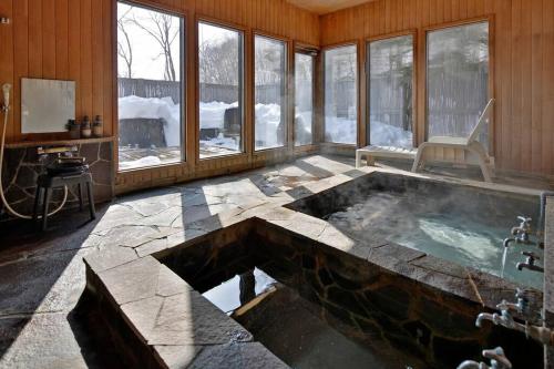 uma casa de banho com banheira de hidromassagem num quarto com janelas em The VILLA ABASHIRI em Kawayu