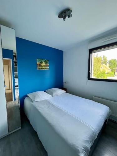 Cette chambre comprend un grand lit blanc et un mur bleu. dans l'établissement La maison d’Emma et son jardin tout près de Lille, à Pérenchies