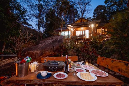 a table with plates of food and a house in the background at ธารทอง ลอดจ์ Tharnthong Lodge in Ban Pang Champi