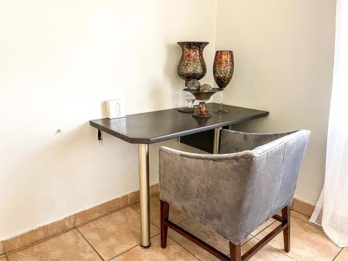 a table and a chair with vases and glasses on it at Bobisemo Luxury Pretoria East Apartment in Tierpoort