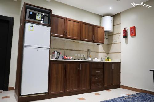 cocina con armarios de madera y nevera blanca en Merfal Hotel Apartments Al Taawan مرفال التعاون, en Riad