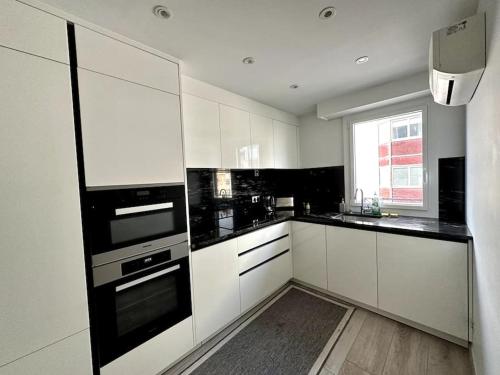 une cuisine avec des armoires blanches et des appareils noirs dans l'établissement Spacieux et Élégant Appartement - Boulogne - Paris, à Boulogne-Billancourt