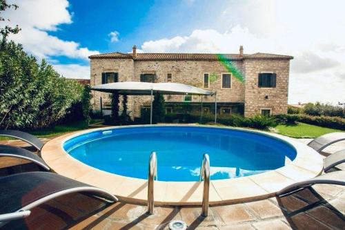 a pool in front of a house with chairs and an umbrella at Ferienhaus in Gesturi mit Whirlpool, Terrasse und Garten in Gesturi