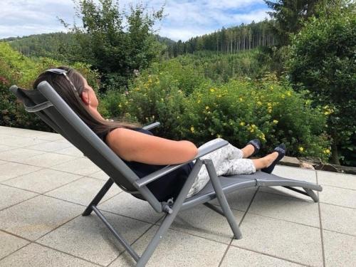 une femme assise sur une chaise longue sur un patio dans l'établissement Chalet BERGglück Willingen, à Willingen