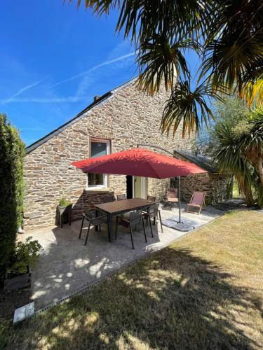 a picnic table with a red umbrella in front of a building at Charmante maison en bord de Rance in Plouër-sur-Rance