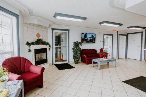 a living room with two red chairs and a fireplace at Western Budget Plus Mosaic Suites in Red Deer