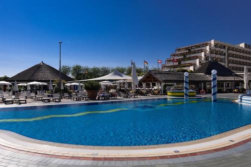 een groot zwembad in een resort met tafels en stoelen bij Aparthotel Holiday in Bibione