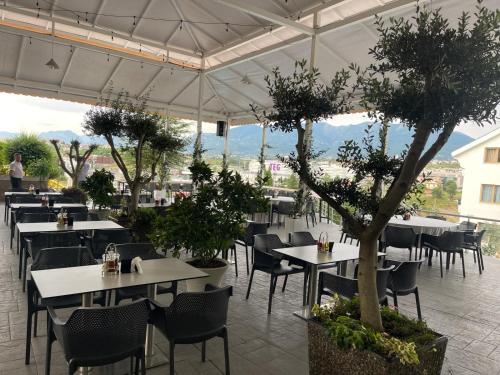 um restaurante com mesas brancas, cadeiras e árvores em Misk Hotel & Resort em Tirana