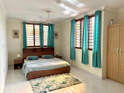 een slaapkamer met blauwe gordijnen en een bed met een tapijt bij Hidden Gem In Oyibi New 2 Luxury Bedroom Apartment in Aburi