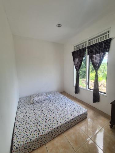 a bed in a room with two windows at Rumah Pemandangan Pegunungan & sawah in Banyumas
