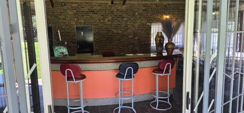 a bar with three stools in front of a counter at Grey lourie Guesthouse in Zeerust