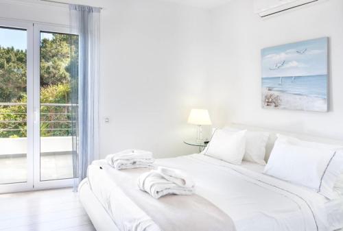 ein weißes Schlafzimmer mit einem großen weißen Bett und einem Fenster in der Unterkunft Villa Coral Luxury Resort in Agios Spyridon
