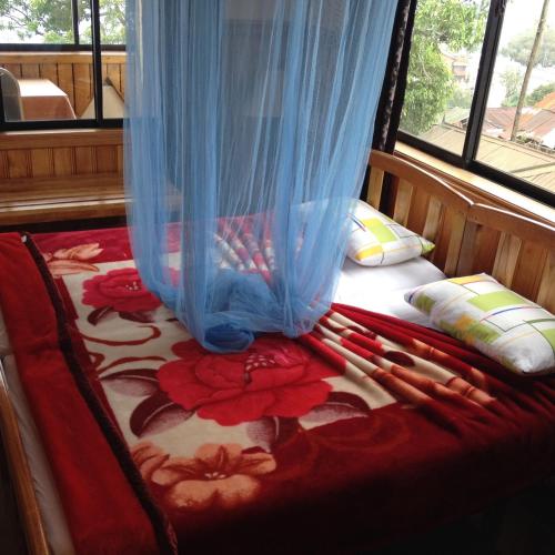 a bed with a blue curtain and red flowers on it at Highcliffe Guest House in Haputale