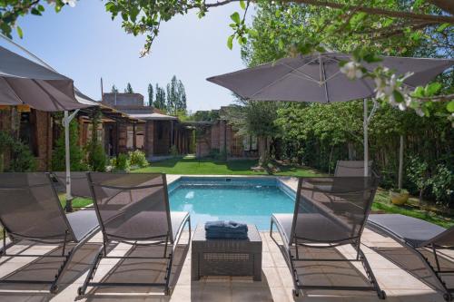 a swimming pool with two chairs and an umbrella at Posada Boutique El Encuentro Chacras de Coria in Chacras de Coria