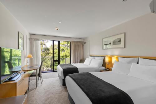 a hotel room with two beds and a desk at Novotel Queenstown Lakeside in Queenstown