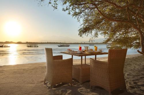 een tafel met stoelen op een strand met het water bij Vamana Resort - CHSE Certified in Gili Trawangan