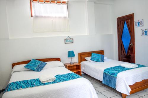 two beds in a room with white walls and blue pillows at Maidith Galapagos Inn in Puerto Ayora