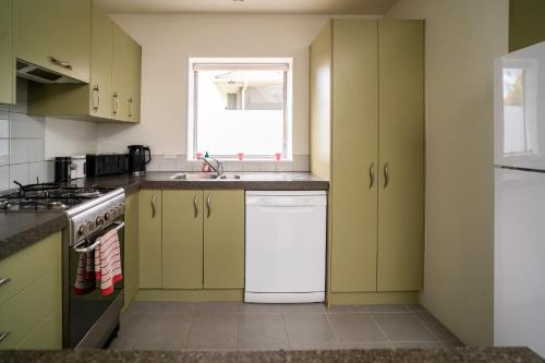 a kitchen with green cabinets and a white dishwasher at Hidden Gem in Rotorua