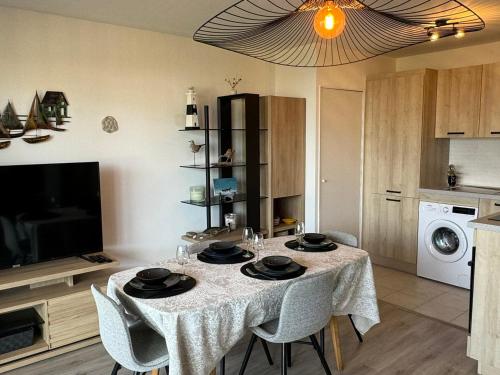 une salle à manger avec une table avec des chaises et une télévision dans l'établissement Charmant 2P avec balcon, proche plage et centre | Parking | Wifi | 4 pers | Cabourg - FR-1-487-365, à Cabourg