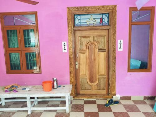 een roze huis met een houten deur en twee banken bij Swastika Residency- Service Apartment -Villa in Tirunallār