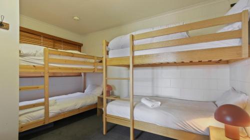 a room with three bunk beds with white sheets at Fountains 6 in Mount Hotham
