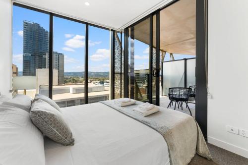 a bedroom with a large white bed with large windows at City Escape Realm 1 BR Apt Wi-Fi Pool Gym SPA in Adelaide