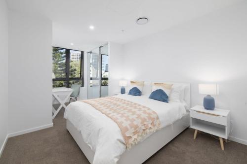 a white bedroom with a large bed and a desk at Surf's Up Stunning Paradise Apartment Serenity in Gold Coast