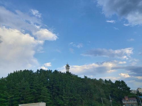 a lighthouse on top of a hill with a cloudy sky at Sokcho Accommodation Bada Bom in Sokcho