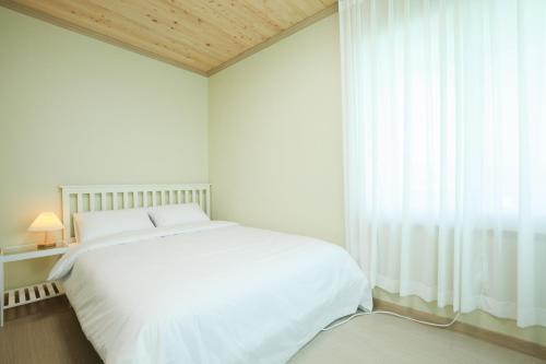 a white bedroom with a white bed and a window at Jeju samdalbada hyang in Seogwipo