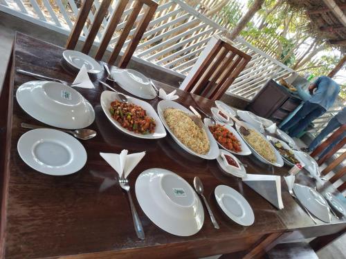 una mesa de madera con platos blancos y cuencos de comida en Rangani Lagoon Resort, en Kalpitiya