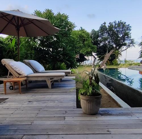a patio with benches and an umbrella next to a pool at JOGLO APONG Beachfront Apartment in Tegallengah