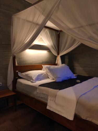 a bedroom with a canopy bed with white pillows at JOGLO APONG Beachfront Apartment in Tegallengah