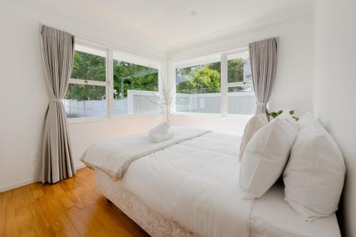 a white bedroom with a large bed with windows at Peaceful Home in the Prime Greenlane in Auckland