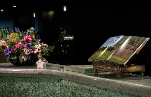 einen Tisch mit einem Buch und einer Blumenvase in der Unterkunft Hotel Rex in Lucca