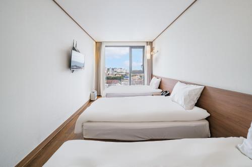 2 camas en una habitación de hotel con ventana en Tamara Jeju hotel, en Seogwipo