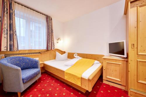 a bedroom with a bed and a tv and a chair at Alpenhotel Rieger in Mittenwald