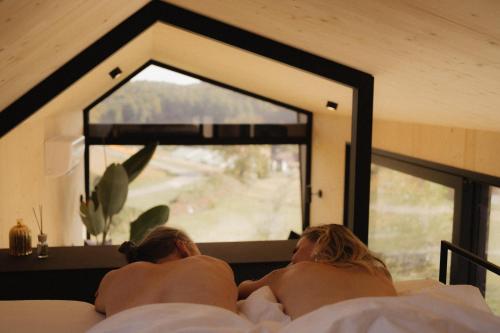 two people laying on a bed looking out a window at Maiers Kuschelhotel Loipersdorf - ADULTS ONLY in Loipersdorf bei Fürstenfeld