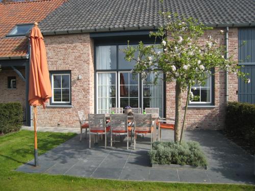 ZuidzandeにあるClassy Holiday Home in Zuidzande with Saunaの家の前にテーブルと椅子と傘
