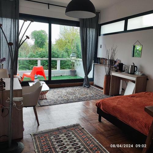 a bedroom with a bed and a desk and a large window at chambre tt confort dans un coin de verdure près de Paris in Le Pecq