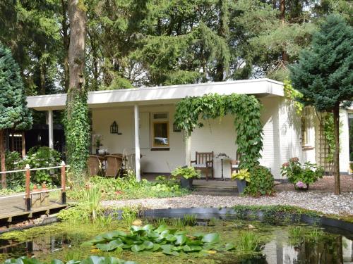 een wit huisje met een vijver ervoor bij A detached bungalow with outdoor fireplace covered terrace and pond in a forest plot in Wateren