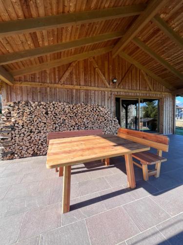 a wooden picnic table on a patio with a pile of logs at Ferienhaus an der Drau in Sankt Oswald