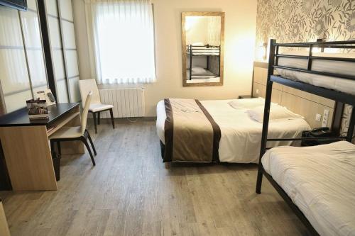 a hotel room with two beds and a desk and a desk at Hôtel Le Bayeux in Bayeux