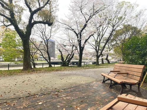 a wooden bench sitting in a park with trees at COCOSTAY銀山町リバーサイド,COCOSTAY Kanayamacho riverside, Great location river view-5 min walk from the nearest station in Hiroshima