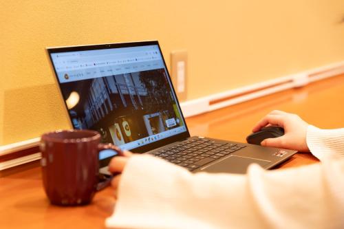 a person sitting at a desk with a laptop and a cup at 城崎温泉 HOSTEL Waraku in Kinosaki