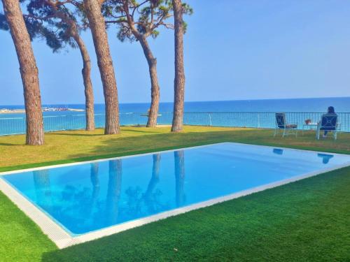 uma piscina com árvores e o oceano ao fundo em Preciosa casa al borde de un acantilado em Arenys de Mar