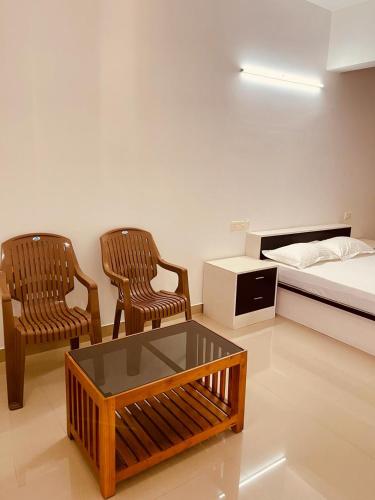 Zimmer mit 2 Stühlen, einem Bett und einem Tisch in der Unterkunft Amalas Lodge in Thiruvananthapuram