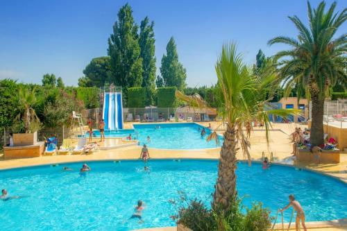 a large swimming pool with people in it with palm trees at Mobilhome au camping Les Salins de La Gardiole ex Camping Europe in Vic-la-Gardiole
