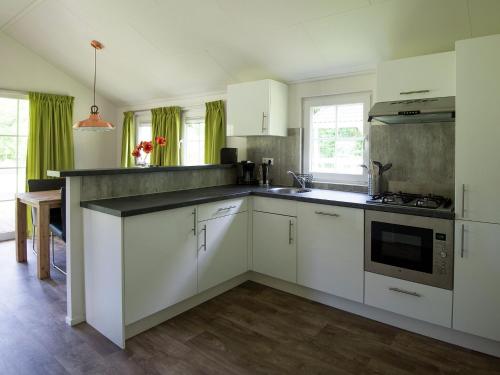 a kitchen with white cabinets and a stove top oven at Cozy lodge with a dishwasher at a holiday park in the Achterhoek in Brinkheurne